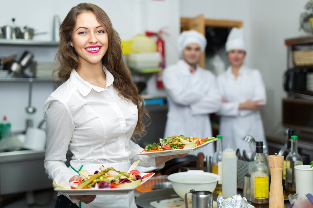 Female waiter taking dish at kitchen